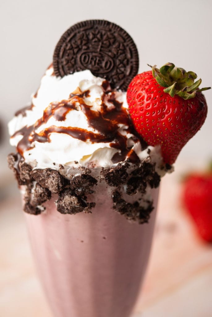 Close up of milkshake garnish with whipped cream, chocolate syrup, and oreo, and a strawberry