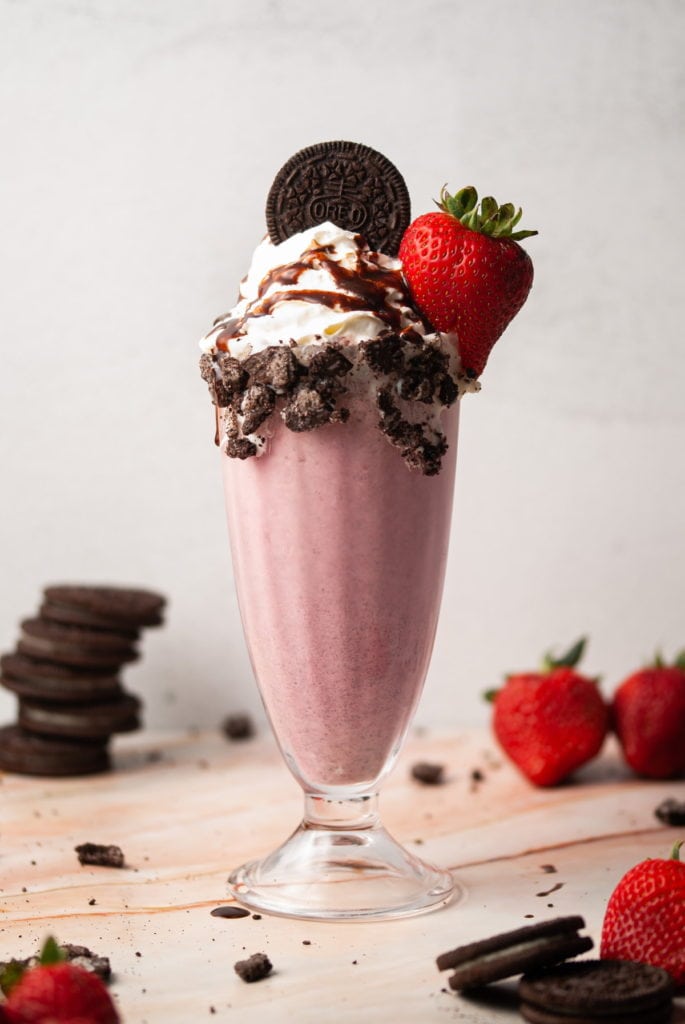 pink milkshake garnished with an oreo and a strawberry