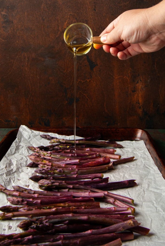pouring oplive oil on asparagus on a baking sheet