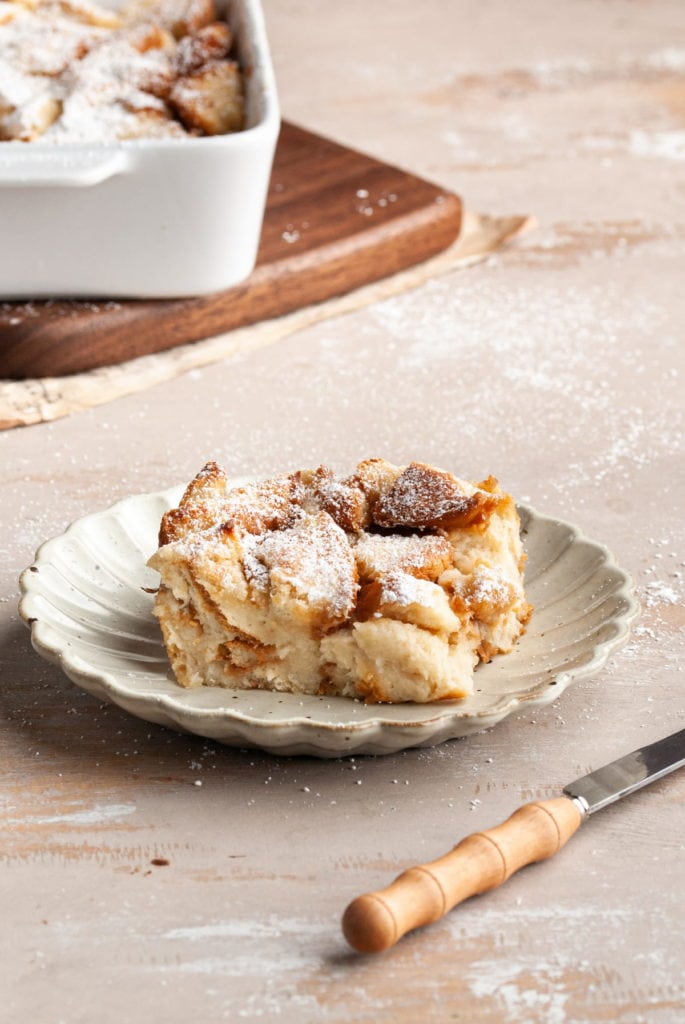 piece of vegan bread pudding on scalloped plate with casserole in the background