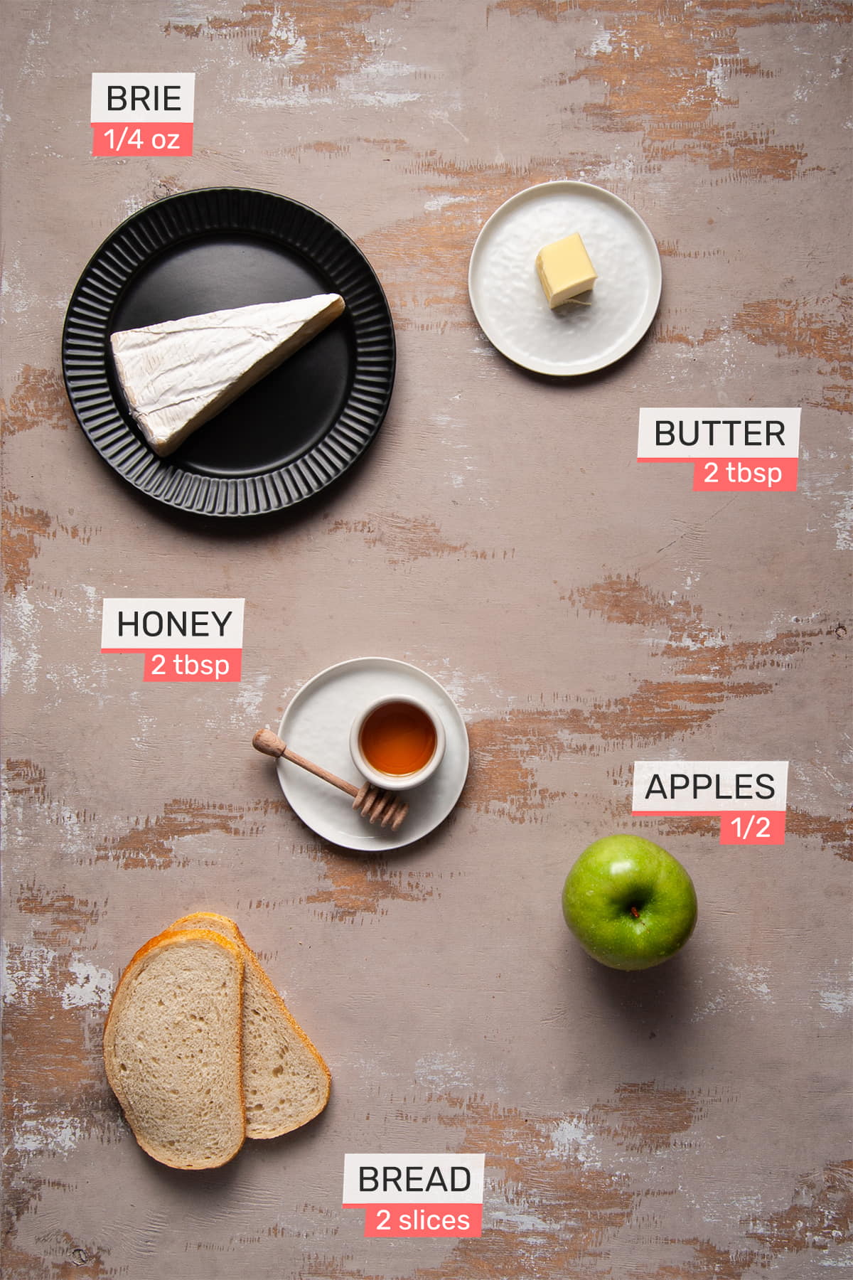 overhead view of all ingredients needed for an apple and brie sandwich on a light wooden background - brie, butter, honey, apple, and bread