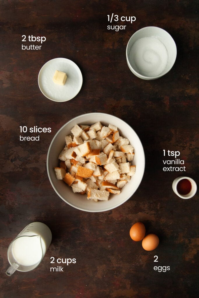 Everything you need to make a simple bread pudding including sugar, butter, cubed bread, vanilla extract, milk, and eggs.