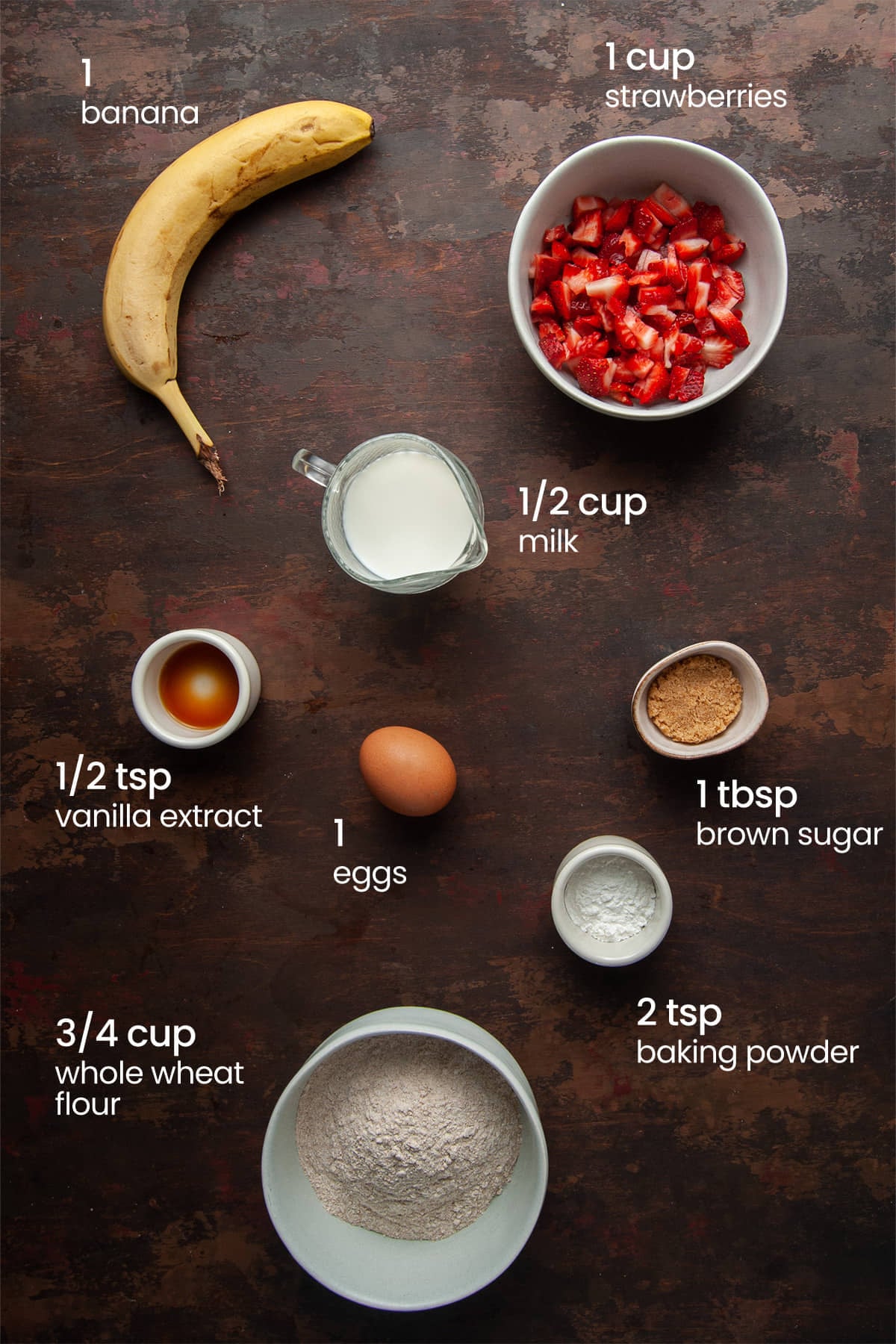 Everything you need to make strawberry banana pancakes including a banana, strawberries, milk, vanilla extract, an egg, brown sugar, baking powder, and whole wheat flour.