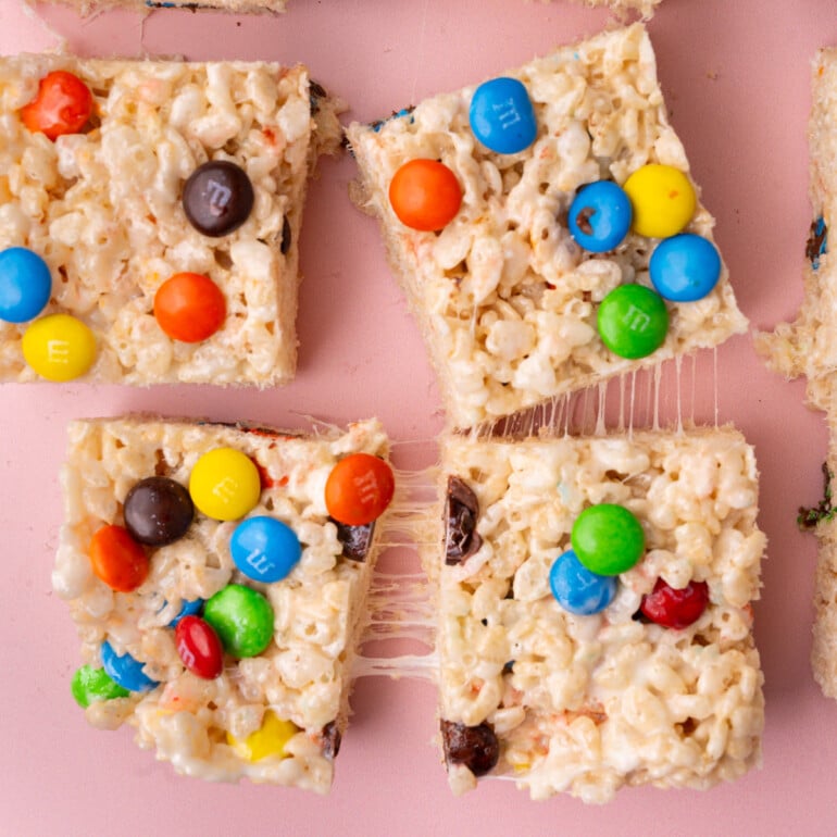 Colorful M&M Rice Krispie Treats on a pink background.