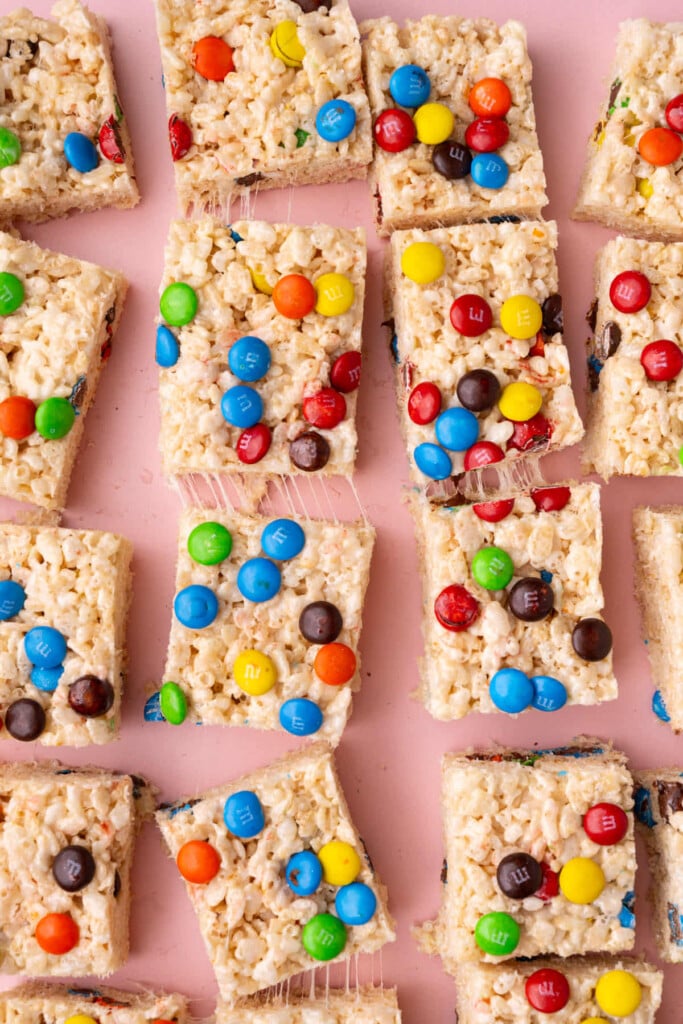 M&M Rice Krispies treats sliced and placed on a pink background. 