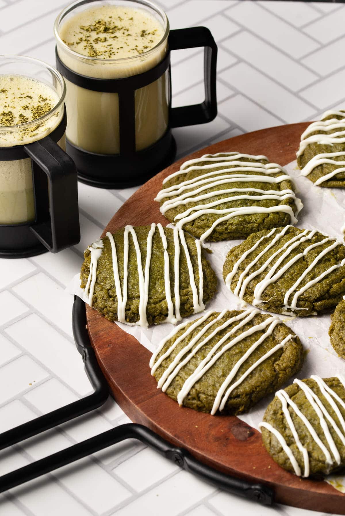 cropped picture of matcha cookies on a round wood board with two matcha lattes in the background