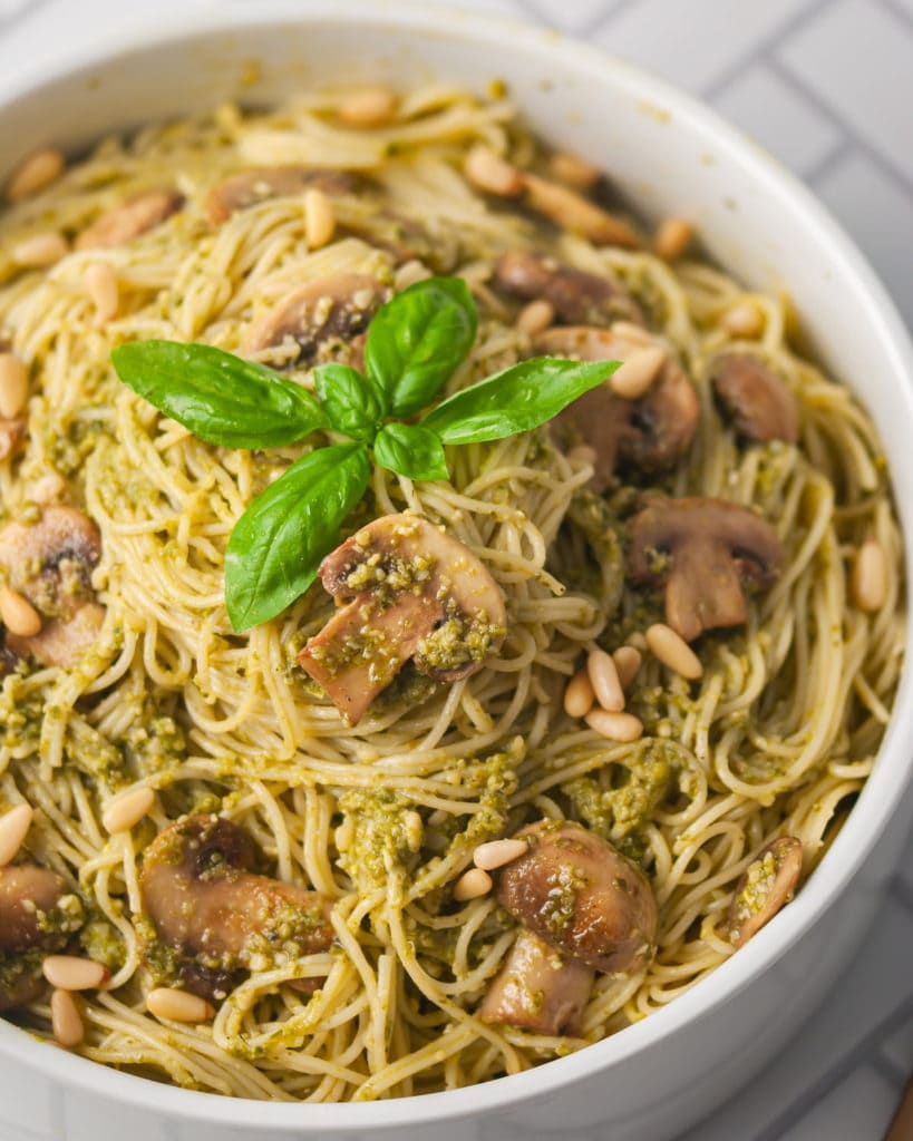 angled picture of angel hair pasta with pesto mushrooms and fresh basil on top