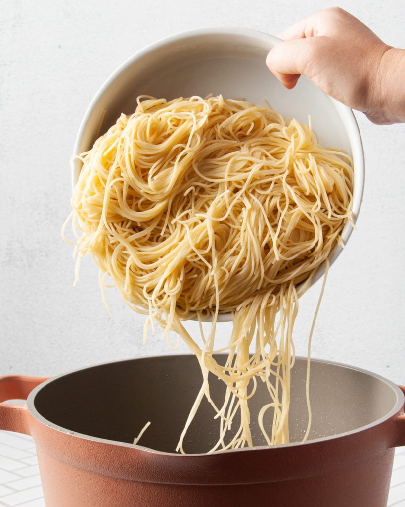 cooked pasta being tipped back into a pot