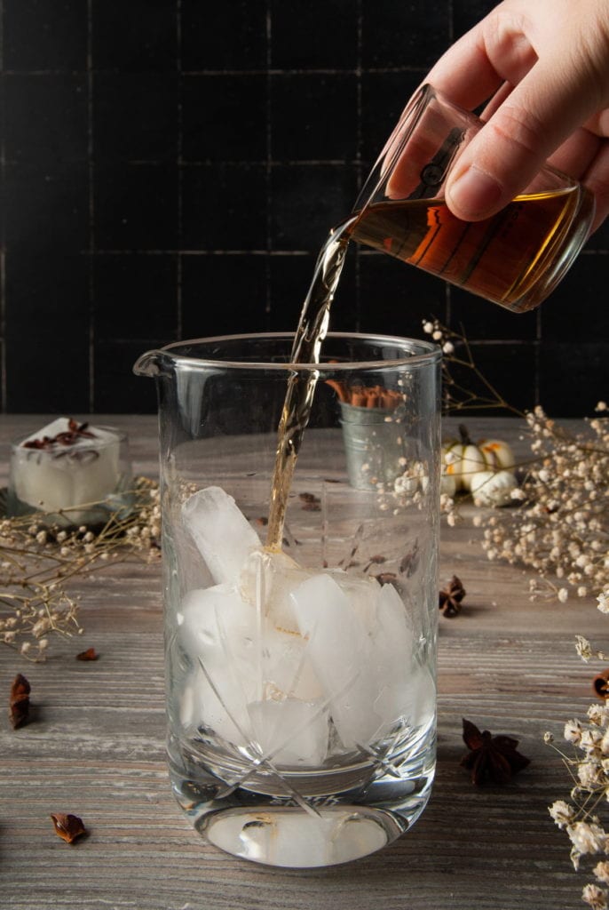 adding whiskey to a cocktail mixing glass