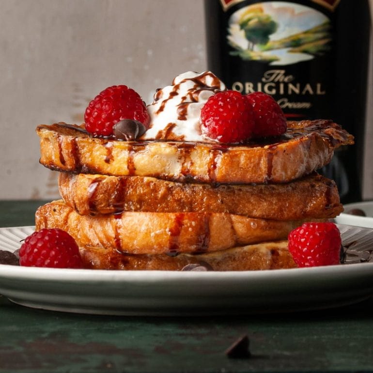 stack of french toast with whipped cream, chocolate syrup, and raspberries