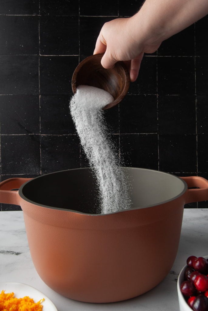 adding sugar to a large pot to make cranberry sauce