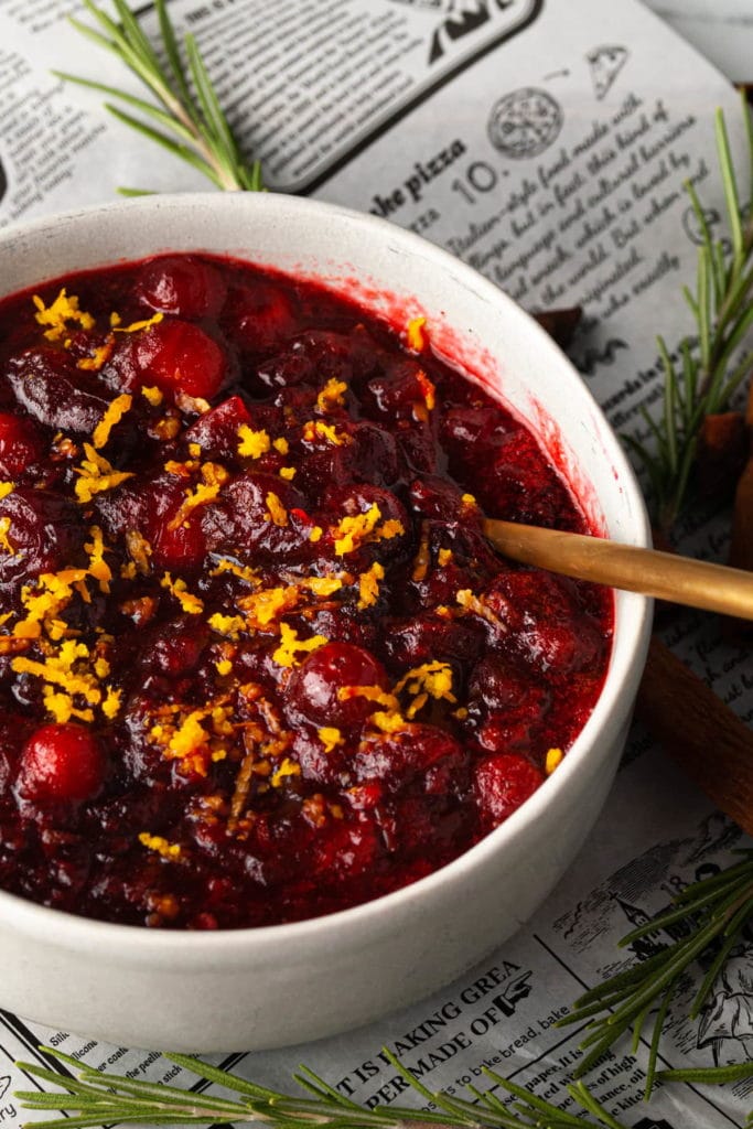 a bowl of cranberry sauce with orange zest sitting on newspaper