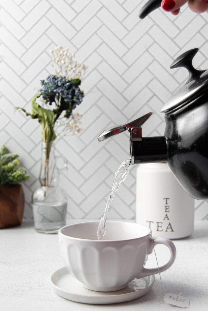 pouring hot water from tea kettle into teacup