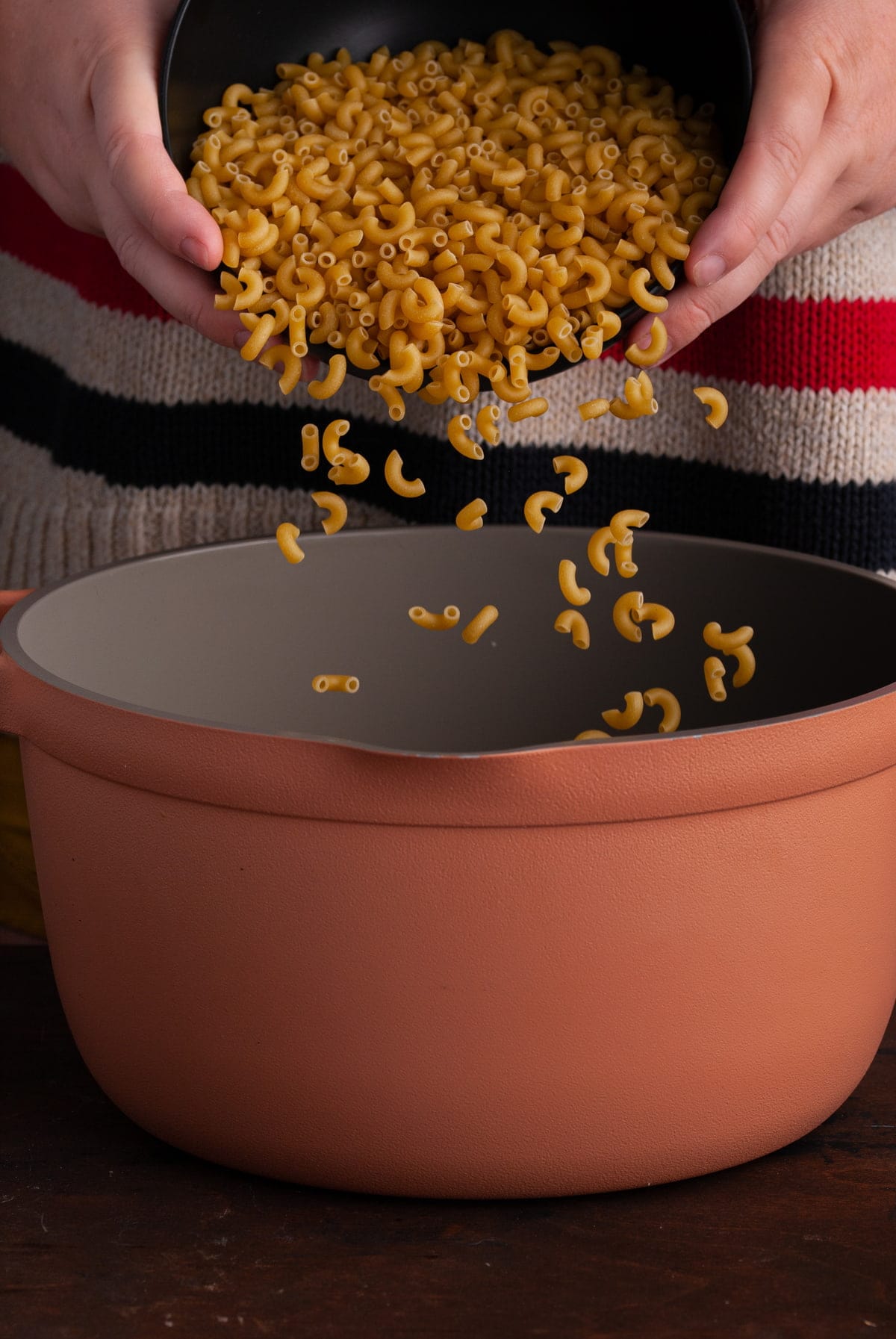 pouring macaroni into a big pot of boiling water