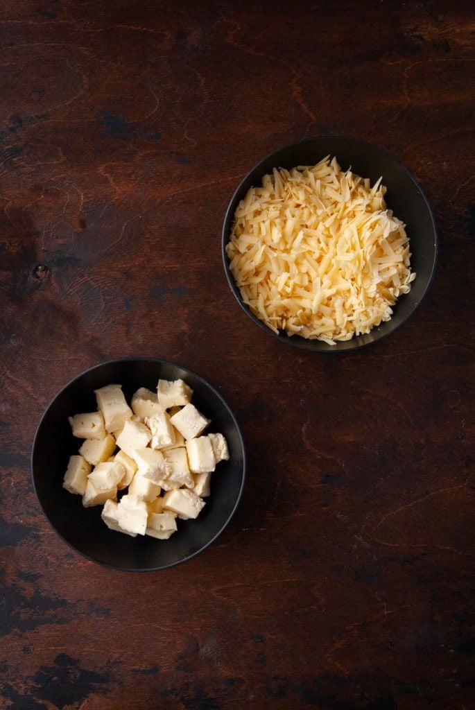 Grated gouda and cubed brie in two bowls.