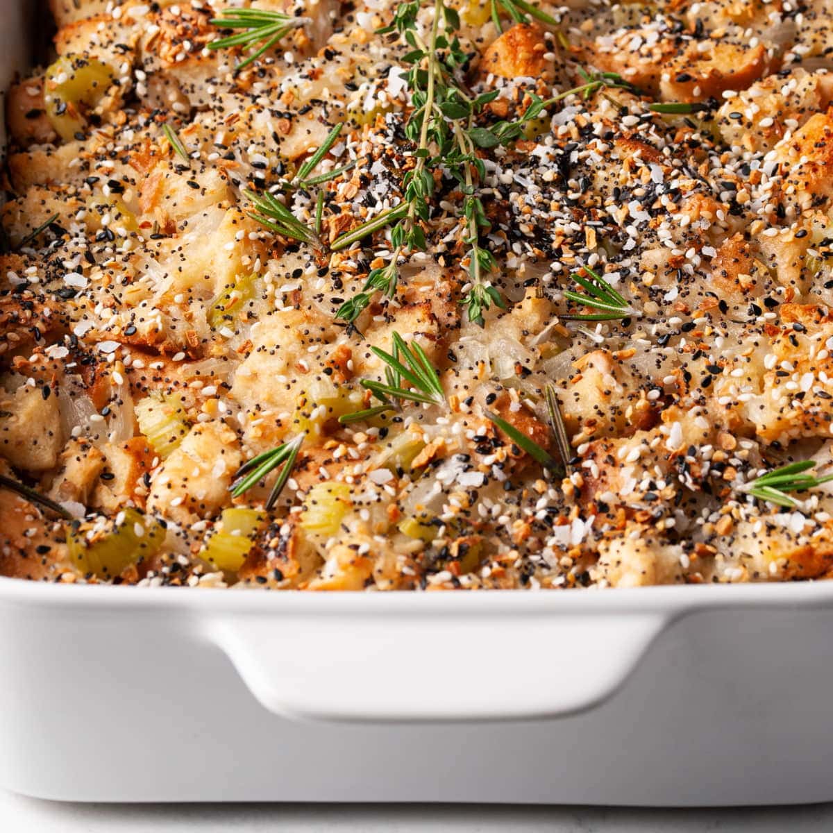 everything bagel stuffing in a casserole dish garnished with rosemary and thyme