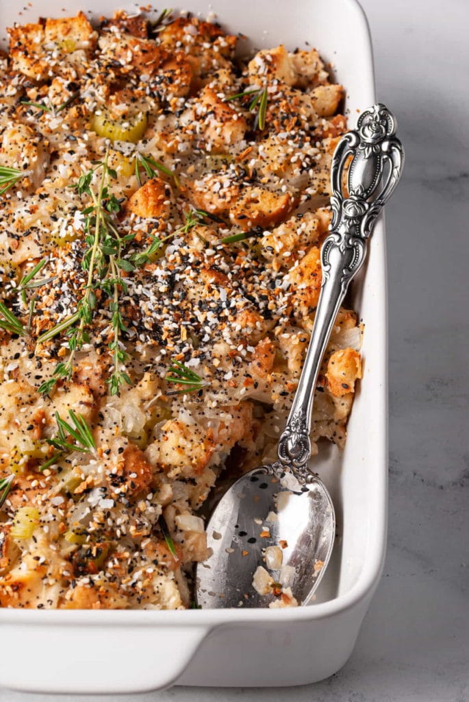 thanksgiving stuffing made with everything bagels in a casserole dish with a serving spoon