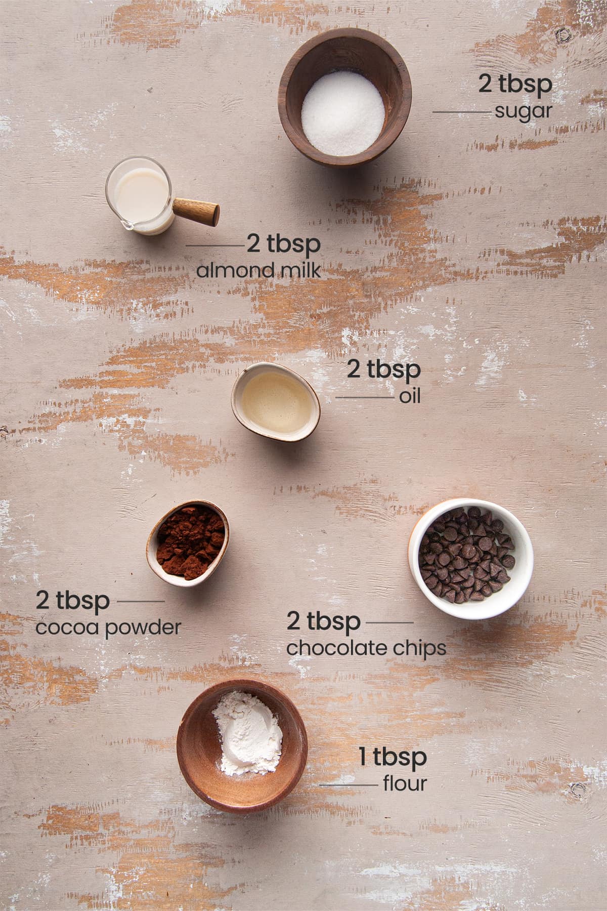 Overhead image of ingredients needed for a fudgy vegan mug brownie - sugar, almond milk, flour, cocoa powder, oil, and chocolate chips.