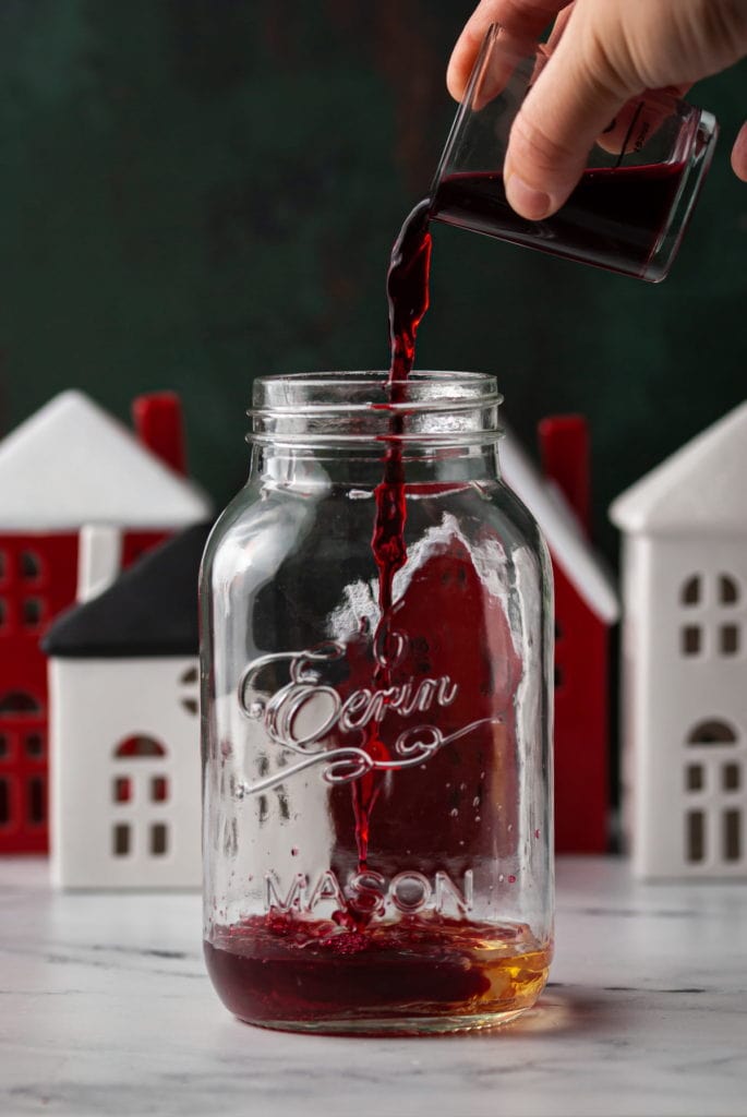 adding cranberry juice to cocktail shaker with christmas town in background