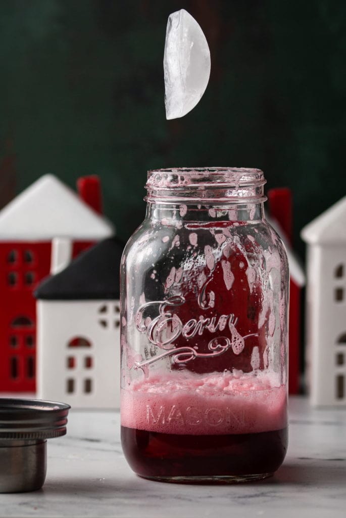 adding ice to cocktail shaker with ingredients for cranberry gin fizz