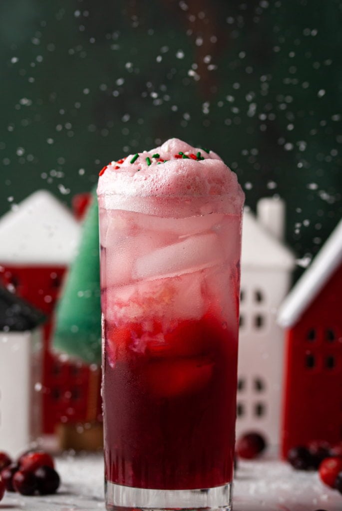 cranberry christmas cocktail in highball glass with snow falling behind it