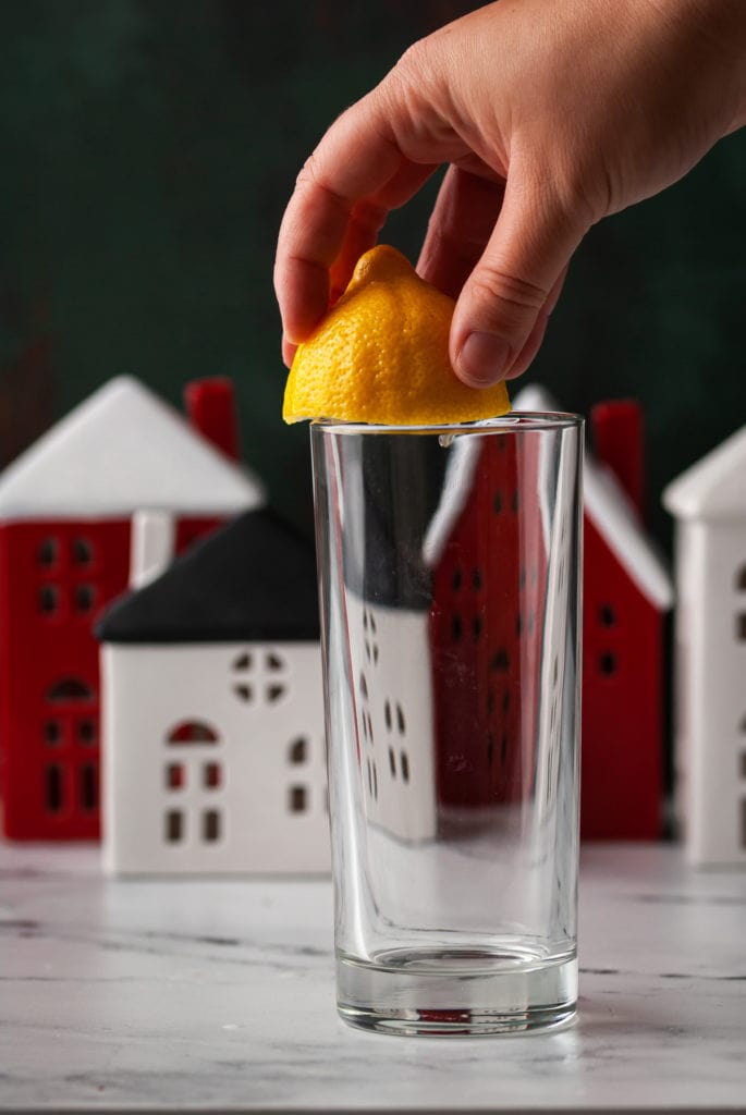 using a lemon to wet the rim of a highball glass for christmas gin cocktail