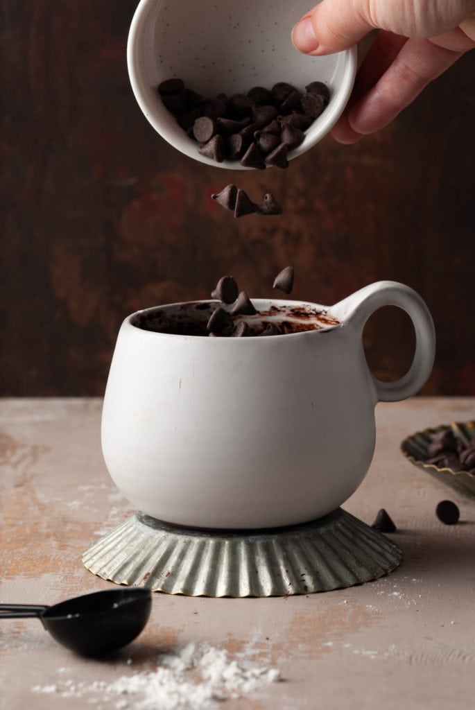Pouring chocolate chips into white mug.