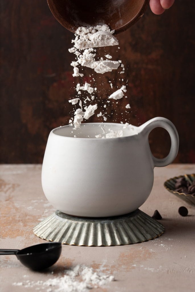 Adding flour to a microwavable mug to make a brownie in.