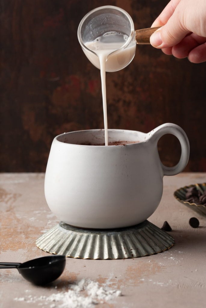 Pouring almond milk into mug to make a single-serving brownie batter.