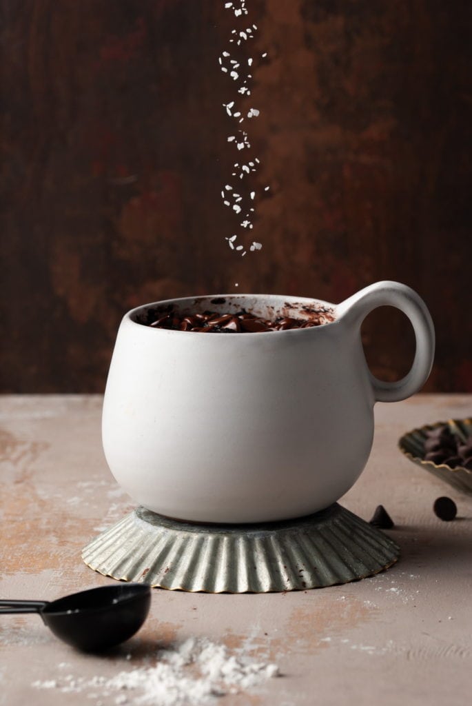 Sprinkling flaky sea salt on chocolate mug dessert.