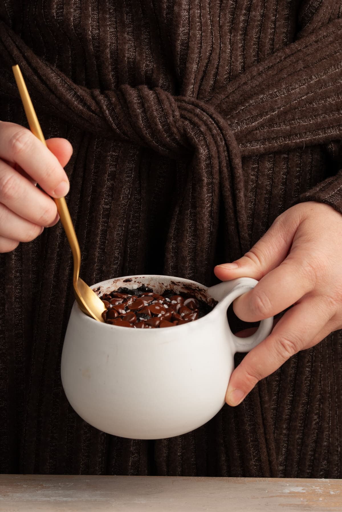 woman holding a chocolate dessert in a mug and taking a bite witha gold spoon