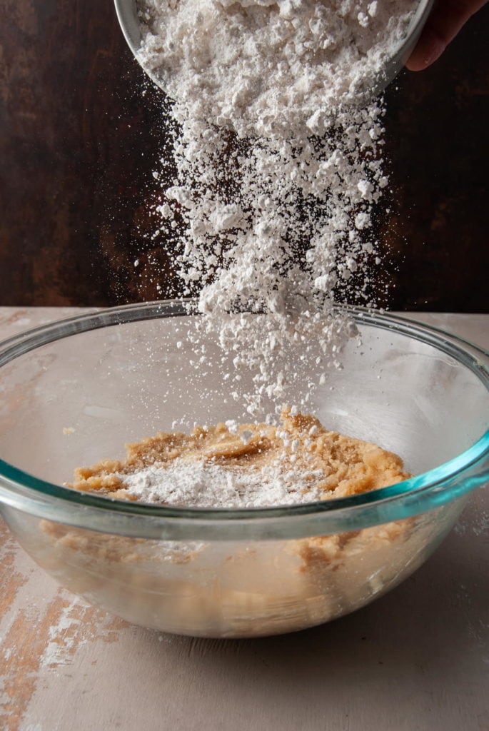 adding dry ingredients to large micing bowl to make cookie cake