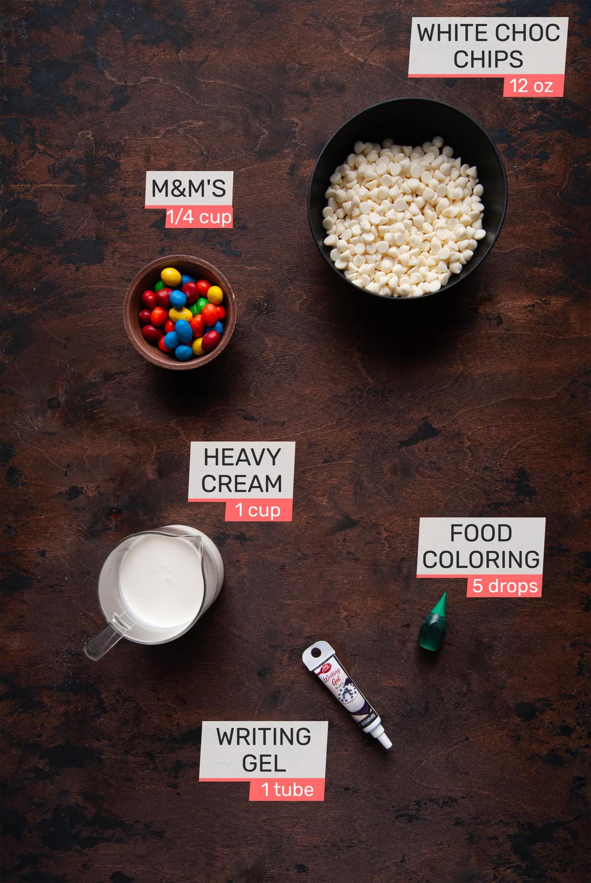 Overhead view of the ingredients for the topping of a Christmas Cookie Cake - M&Ms, white chocolate chips, heavy cream, green food coloring, and black writing gel.