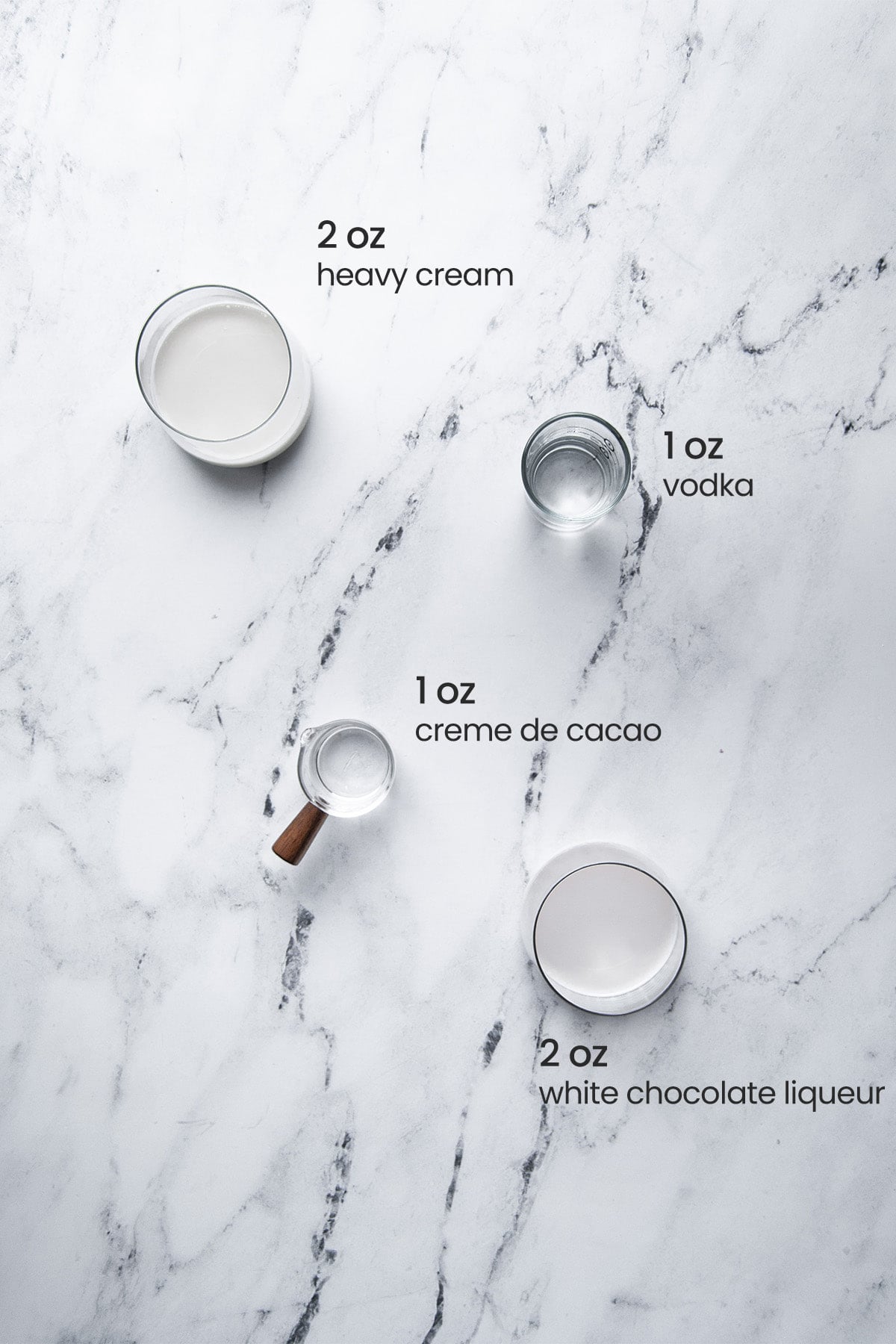 Overhead view of the ingredients needed for a white chocolate martini - heavy cream, vodka, creme de cacao, and white chocolate liqueur.