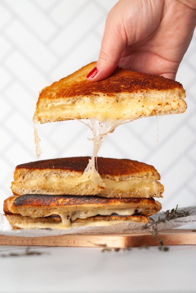 a stack of 4 halved grilled cheese with hand picking up the top half