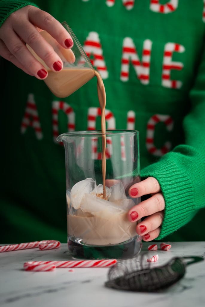 pouring chocolate liqueur into cocktail mixing glass with ice with christmas decor