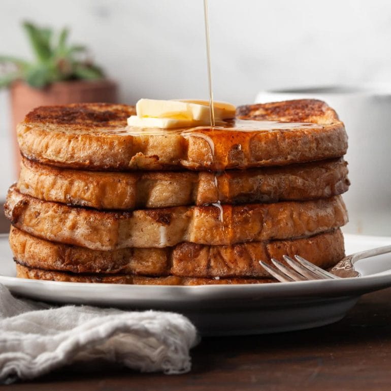 stack of french toast with butter on top and syrup being drizzled on