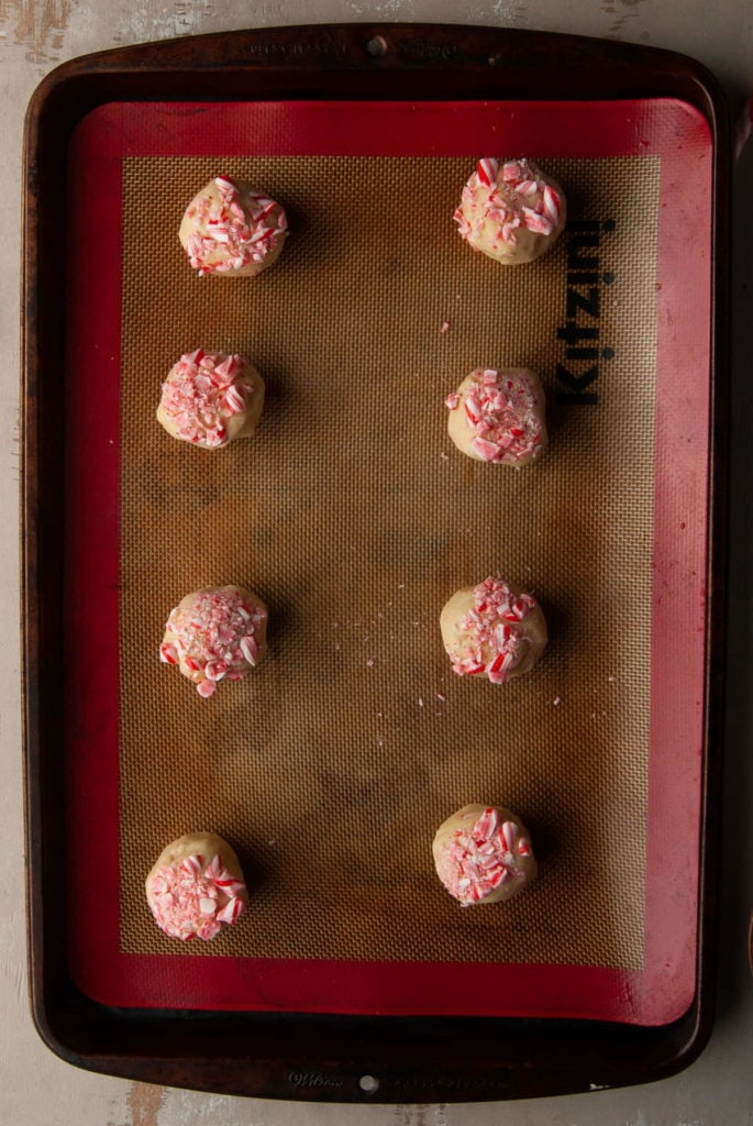 8 candy cane shortbread cookie dough balls lined up on a reusable baking sheet
