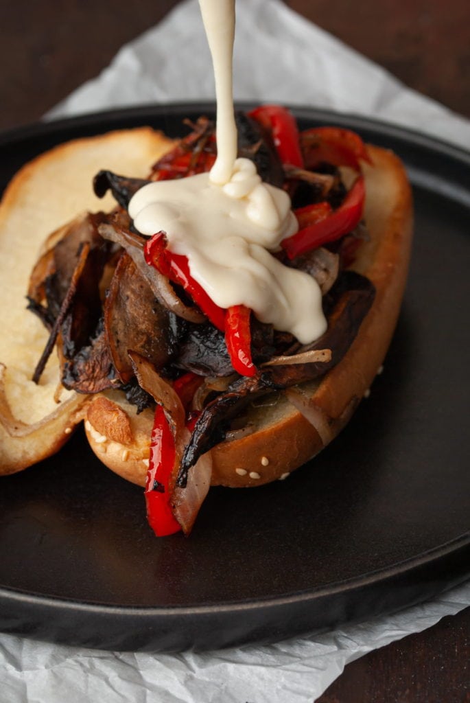 pouring homemade cheese sauce on vegetarian philly cheesesteak