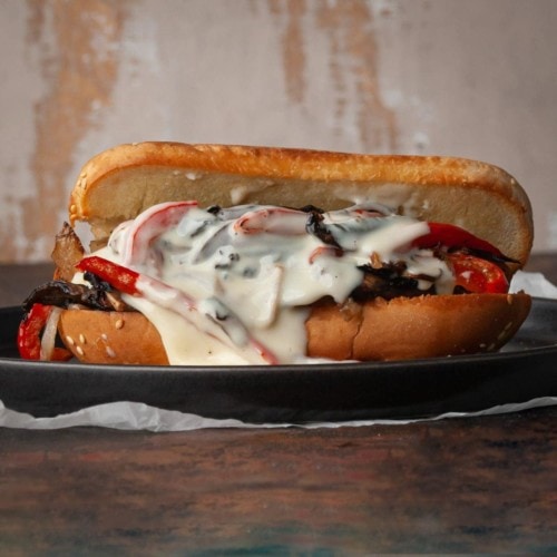 vegetarian philly cheesesteak with cheese sauce oozing out on hoagie roll