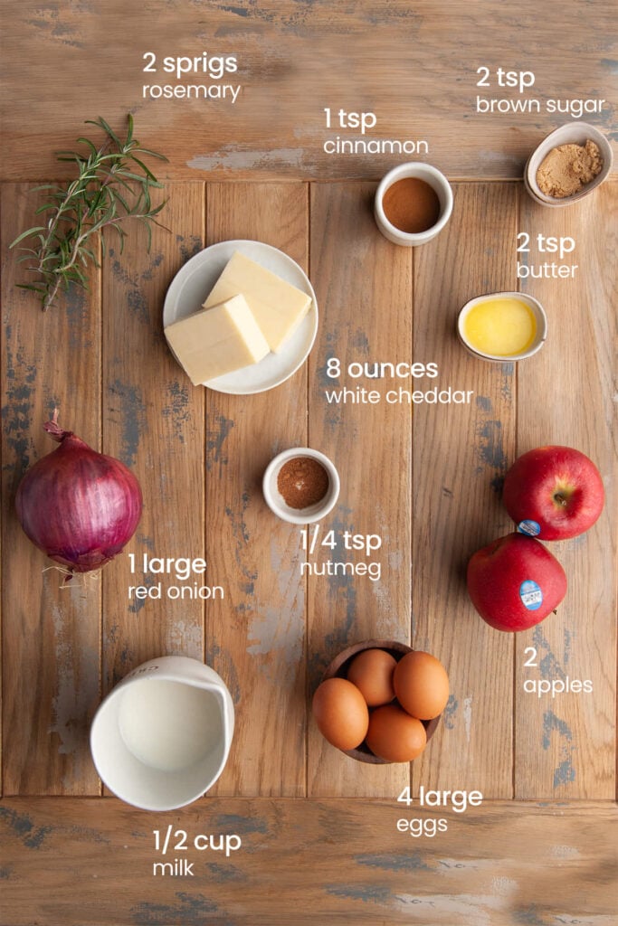 Everything you need for the filling for apple cheddar quiche including rosemary, cinnamon, brown sugar, white cheddar cheese, melted butter, red onion, nutmeg, apples, milk, and eggs.