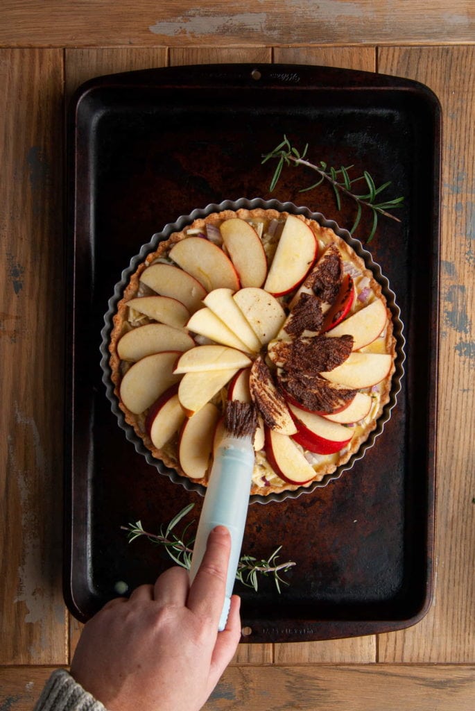 using a pastry brush to add cinnamon sugar and butter mixture to top of apples on  quiche