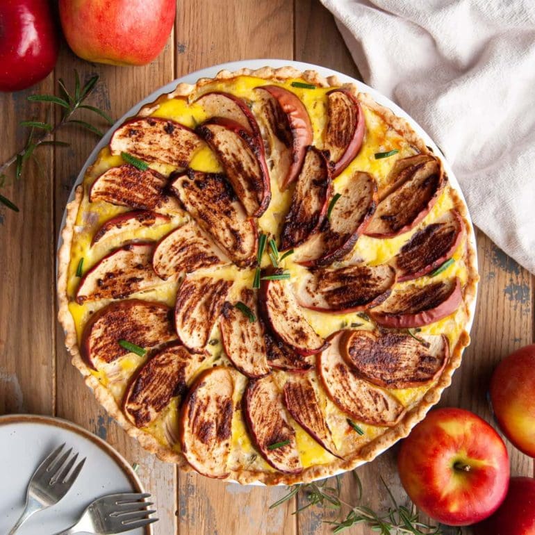 Sweet and Savory Apple and Cheddar Quiche with the top layer being artfully placed sliced apples topped with cinnamon and sugar