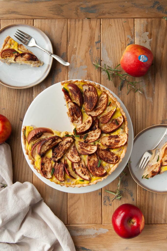 overhead shot of an apple and cheddar quiche with two slices cut out of it and on little plates on either side of the quiche