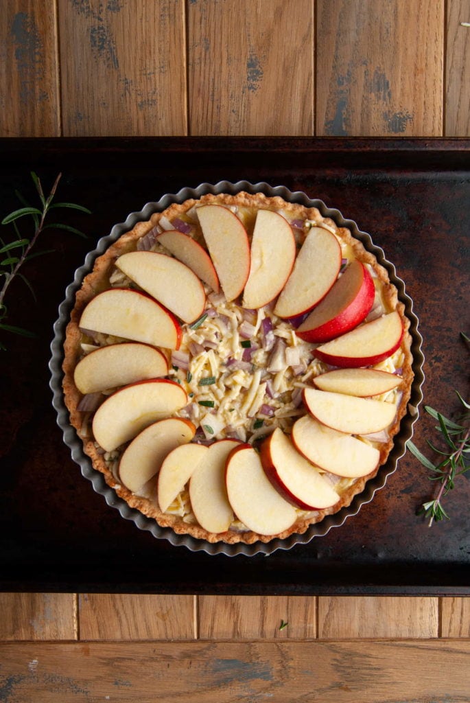 arranging apple slices in a circle close to the edge on an apple and cheddar quiche