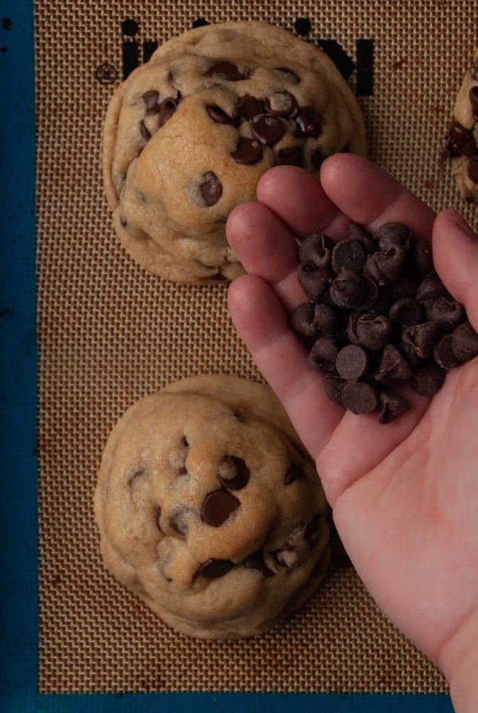 grabbing a handful of chocolate chips to press into top of baked chocolate chip cookie