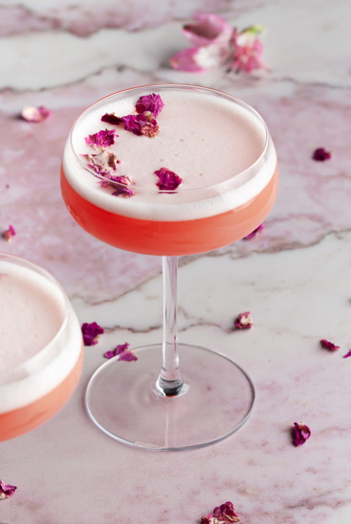 pink cocktail with airy white foam and rose petals