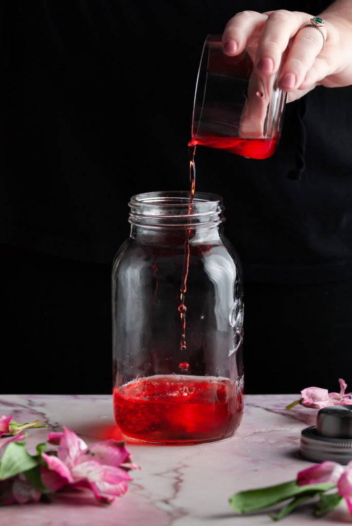 adding aperol to a cocktail shaker surrounded by flowers