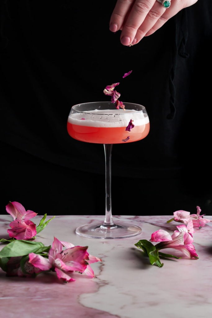 garnishing a pink cocktail with rose petals