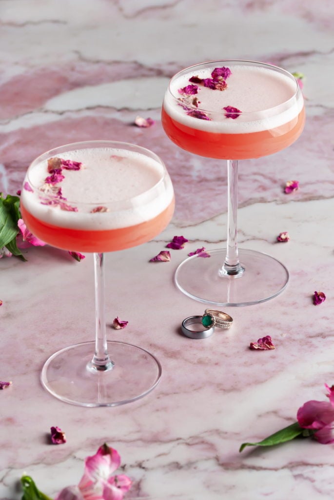 2 romantic pink cocktails with wedding rings between them